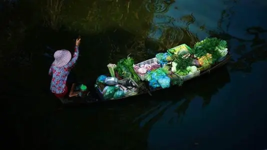 Une vendeuse se dirige vers le marché pour y vendre ses légumes. L'impression que l'eau est en train de dormir. 